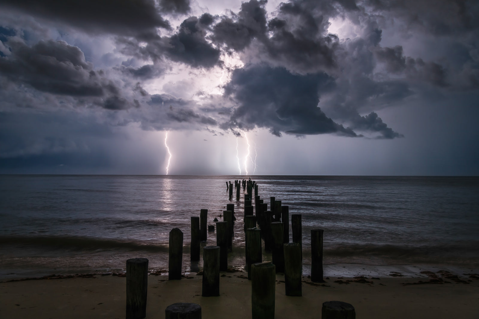 Fine art print of Lightning Bolts, rain clouds, and the old pilings in Naples, Florida – landscape photography by Andrew Mease