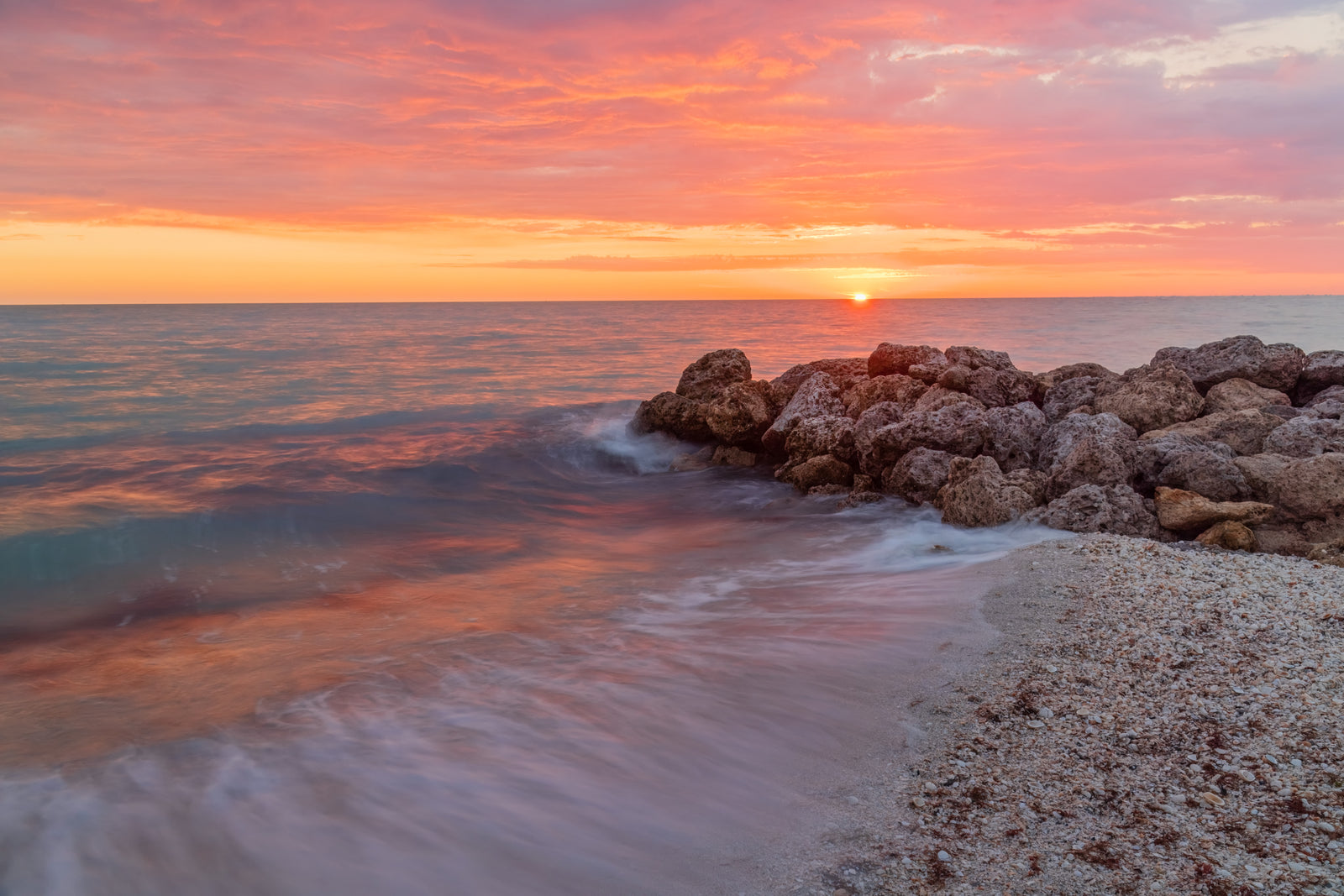 Fine art print of a warm pink and orange colored sunset on Little Hickory Island in Bonita Springs, Florida next to the rocks – landscape photography by Andrew Mease